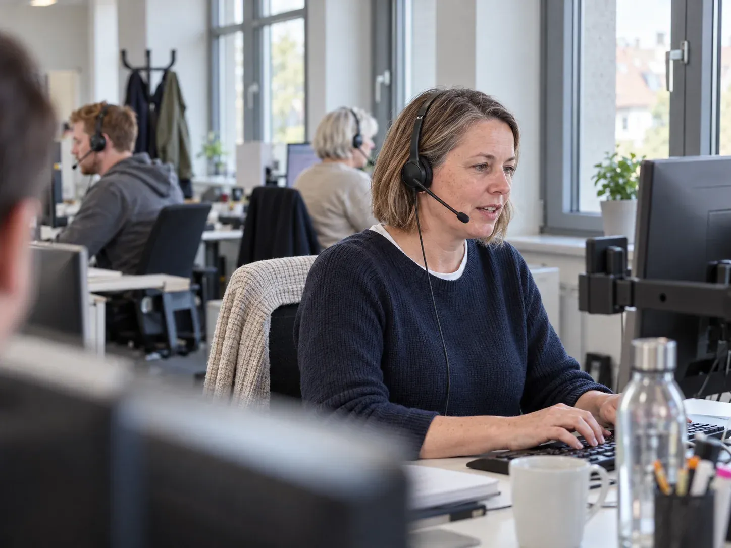 Freundliche Mitarbeiterin einer Telefonzentrale mit Headset am Arbeitsplatz.